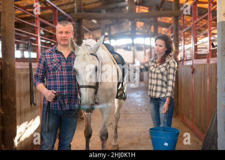 Ein paar Bauern mit Eimer vor dem Pferd stehen an der Stallung Stockfoto