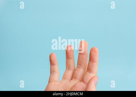 Tropfen Blut auf den Finger eines Kindes. Das Konzept der Messung des Blutzuckerspiegels mit Hilfe von Streifen. Blauer Hintergrund Stockfoto