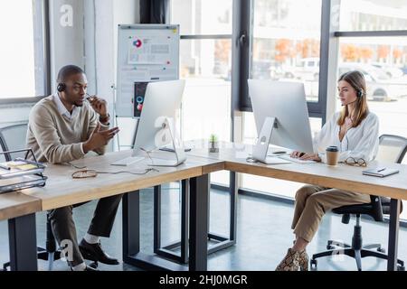 Interrassische Mitarbeiter in Headsets, die in modernen Büros arbeiten Stockfoto