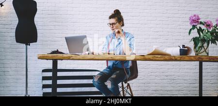 Junge Schneiderin surft im kreativen Workshop im Internet auf dem Laptop Stockfoto