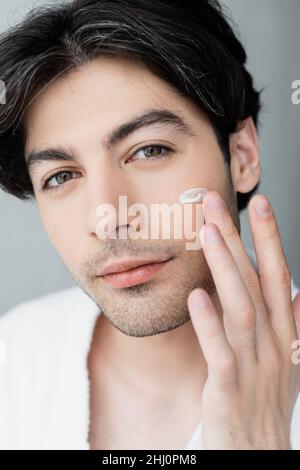 Nahaufnahme eines jungen Mannes, der Gesichtscreme anwendet und die Kamera anschaut Stockfoto