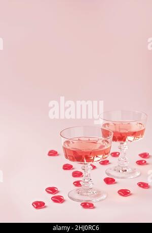 Zwei Kristallgläser mit Rosenperlwein oder Champagner und roten Glasherzen auf pastellrosa Hintergrund. Happy Valentines Day Konzept. Minimale kreative Komposition mit Kopierplatz. Stockfoto