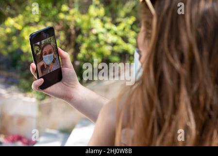 Nicht erkennbare Frau mit Gesichtsmaske nutzt Smartphone, um Selfie zu machen. Stockfoto