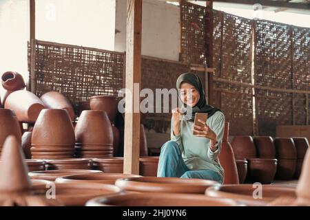Happy muslim Mädchen in Hijab zwischen Keramik während der Verwendung von Handy Stockfoto