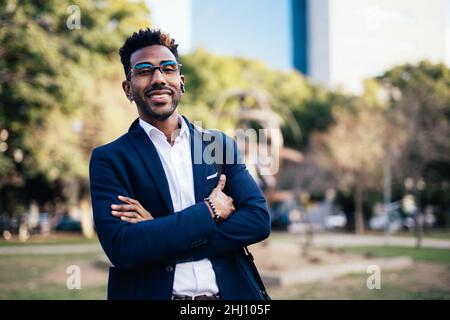 Porträt eines lächelnden Geschäftsmannes und einer Brille auf der Straße mit gekreuzten Armen Stockfoto