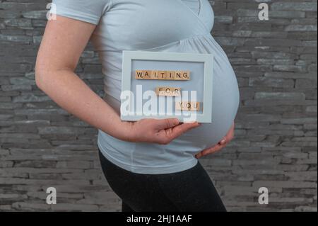 Eine Schwangerin im Jahr 30s hält ein Schild vor ihrem Bauch Stockfoto