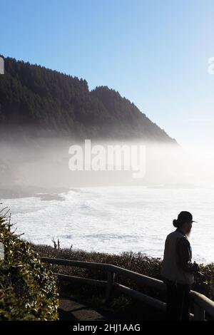 Ein Mann blickt auf den Ozean, wo eine niedrige Nebelschicht in der Nähe von Yachats, Oregon, USA, schwebt. Stockfoto