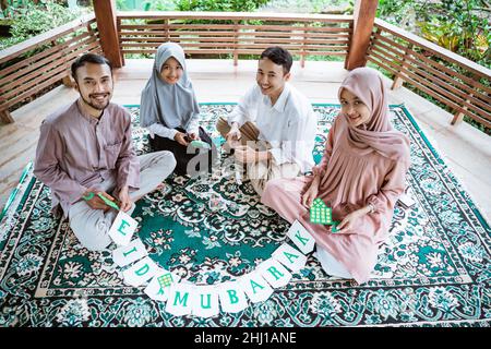 Muslimische asiatische Familie sitzt auf dem Teppich und macht Papierdekorationen Stockfoto