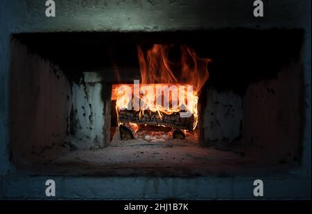 Russischer Retro-Ofen, in dem Feuerholz in einem Dorfhaus brennt. Den Ofen zum Kochen anzünden. Traditionelle Küche. Stockfoto