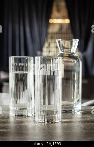 Zwei Gläser und ein Glaskrug mit Wasser stehen auf dem Steintisch des Restaurants. Vertikales Foto