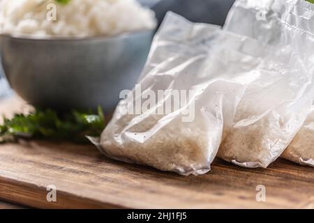 Roher Reis in Plastiktüten auf Holzhintergrund und gekochter Reis in einer Schüssel. Stockfoto