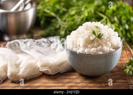 Gekochter Reis in einer Schüssel mit rohem Reis in Plastick-Tüten. Stockfoto