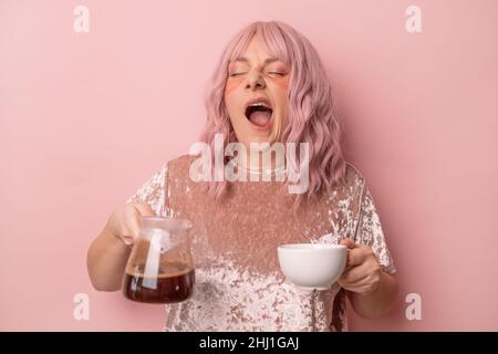 Schläfrige müde Frau will schlafen, sich erschöpft fühlen, gähnend, früh isoliert auf rosa Hintergrund aufwachen. Mädchen hält eine Glas Teekannen Tee und eine Tasse Stockfoto