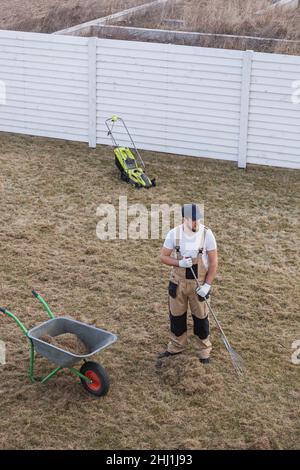 Der Mensch-Gärtner, der den Rasen mit Rechen und Schreckgespenst erschreckt, schreckt den Rasen und entfernt altes Gras Stockfoto