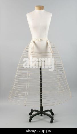 Crinolin ca. 1860 American dieser Petticoat besteht aus Metalldraht und Baumwollband. Es wäre mit einem zusätzlichen Stoffpetticoat überzogen worden, um das darüber getragene Kleid zu schützen. Das Heben von Käfigkrinolinen könnte aus Whalebone, Rohr oder Stahl bestehen. Das konzentrische Skelett des Käfigs würde mit Stoffbändern zusammengehalten oder vollständig in Stoff gehüllt werden. Die Weite, die mit dieser Unterkonstruktion erreicht werden konnte, war sogar größer als die von Fahrradtaschen aus dem 18. Jahrhundert. Crinoline. Amerikanisch. Ca. 1860. Metall, Baumwolle Stockfoto
