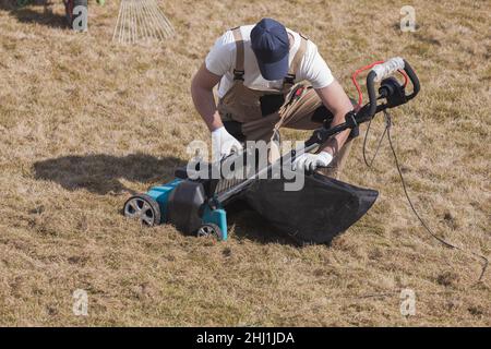 Mann Gärtner Reinigungsmaschine scarifier von alten trockenen Gras auf dem Rasen Stockfoto