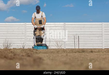 Der Mensch-Gärtner, der Rasen mit einem Vertikutierer erscharft, erscharft den Rasen und entfernt altes Gras Stockfoto
