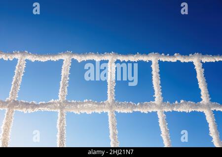 Verschneite, gefrorene Metallzaun aus nächster Nähe. Winter verschneit Wetter. Alte ländliche Zaun mit kleineren Löchern mit Schnee bedeckt. Wolkiger, kalter Tag. Eiskalt im Winter Stockfoto