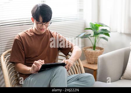 Technologiekonzept der Mann mit seinem lässigen T-Shirt und Jeans sitzt bequem auf dem Holzstuhl und macht einen Touchscreen, um die Webbrowsen zu überprüfen Stockfoto