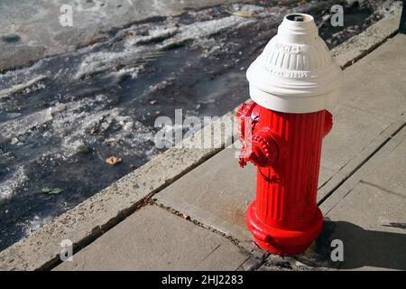 Ein traditioneller rot-weißer alter Hydrant mit Eis und Schnee auf dem Boden an einem sonnigen Wintertag Stockfoto