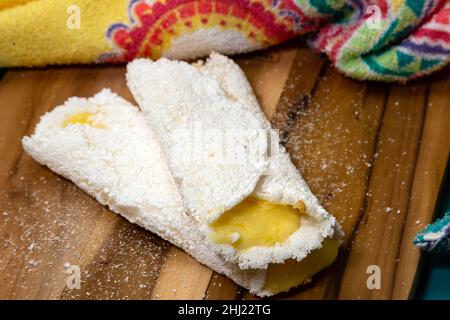 Goiania, Goias, Brasilien – 26. Januar 2021: Zwei Tapiocas gefüllt mit Käse auf einem Holzbrett mit einem gemusterten Stoff Detail. Stockfoto