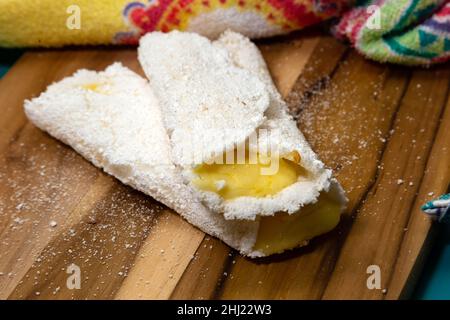 Goiania, Goias, Brasilien – 26. Januar 2021: Zwei Tapiocas gefüllt mit Käse auf einem Holzbrett mit einem gemusterten Stoff Detail. Stockfoto