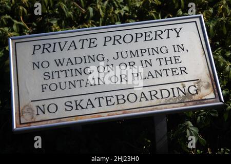 Privateigentum, kein Planschreiten, Hereinspringen, Sitzen auf oder im Springbrunnen oder Pflanzgefäß und kein Skateboarding Eisenschild an einem Garten an einem sonnigen Tag Stockfoto