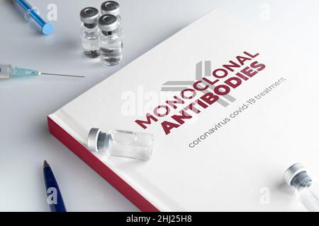 Konzept monoklonaler Antikörper: Ein Buch auf einem weißen Tisch mit einigen Fläschchen und Spritzen Stockfoto