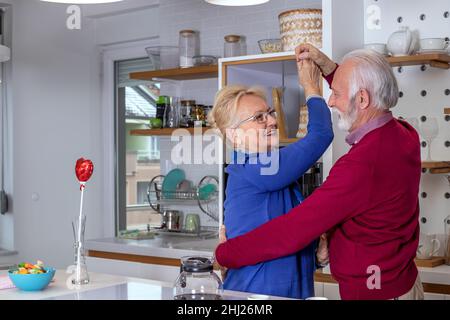 Glückliches Seniorenpaar, das in der Küche tanzt. Der Ehemann gratuliert seiner Frau zum Valentinstag oder zum Hochzeitstag. Stockfoto