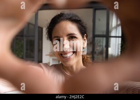 Das Gesicht der Frau sieht durch verbundene Finger, die eine Herzform zeigen Stockfoto