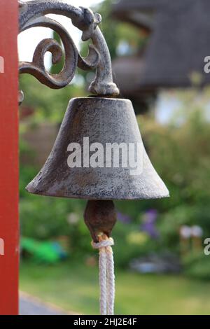 Alte verwitterte traditionelle gusseiserne Glocke, die vor einem Gebäudeeingang hängt Stockfoto