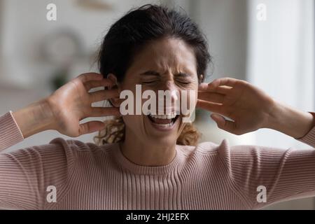 Schreiende Frau stopft mit Fingern Ohren verärgert durch Lärm Stockfoto