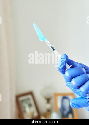 Arzthand mit einer Original-Spritze mit blauem Adapter und Covid-19-Impfstoff in einem Haus Stockfoto