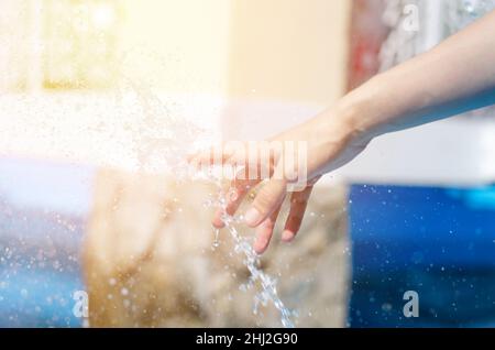 Die weibliche Hand berührt den Sprühnebel des Brunnens. Die Hand der Frau im Brunnen Stockfoto