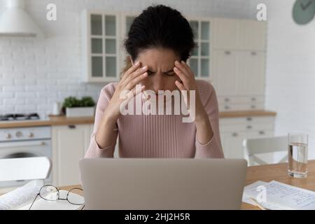 Müde junge Frau fühlt sich unwohl, während sie in der Nähe des Laptops sitzt Stockfoto