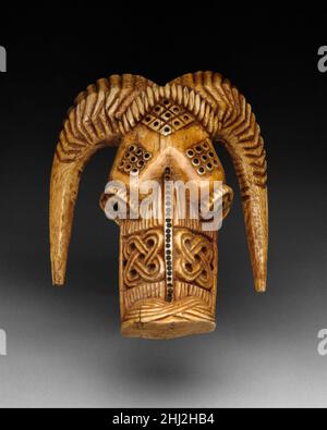 Orufanran Kostümzubehör: RAM Head 17th–19th Century Yoruba people, Owo Group der Kopf dieses winzigen Elfenbeinrammers war Teil der höfischen Insignien eines Olowo, des Herrschers des Yoruba-Staates Owo im Süden von Nigeria. Es wurde als dekoratives Element eines orufanran geschaffen, eine Art zeremonielles Ensemble, das von den Olowo und hochrangigen Chefs während staatlicher Zeremonien getragen wurde. Der orufanran bestand aus einem sperrigen Mantel oder Hemd, das mit roten Flanellschuppen bedeckt war, und war mit Elfenbeinbildern von menschlichen Gesichtern und den Köpfen von Krokodilen, Leoparden und Widdern übersät. Das Outfit bezieht sich auf das militärische du des Chefs Stockfoto