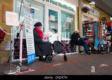 Ältere Männer und Frauen, die vor der Praxis eines Chiropodisten in Morecambe lancashire warten, tragen beide Gesichtsbezüge Stockfoto