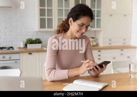Frau hält Smartphone und Bleistift, überprüfen Zeitplan Haushaltsplanung Stockfoto