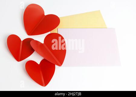 Grußkarte zum Valentinstag. Umschläge auf weißem Hintergrund und rote Kunststoffherzen. Kopierbereich. Stockfoto