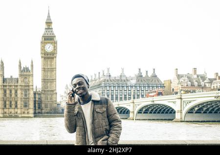 afroamerikanischer junger Mann mit Handy am Ufer der Themse in London - Hipster-Mann-Modell mit modernem Handy-Smartphone Stockfoto
