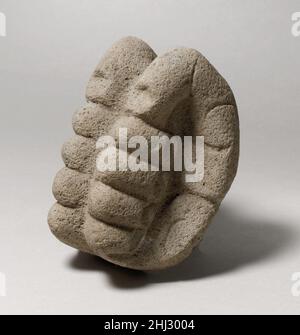 Hacha in Form gebundener Hände 4th–7th Jahrhundert Veracruz Diese Skulptur aus vulkanischem Stein nimmt die Form zweier überlebensgroßer Hände mit geballten Fäusten an. Die Hände werden mit den Fingern nach außen hin zurück an den Rücken gelegt. Auf jeder Seite sinken die Finger in einer geraden Linie zur Handfläche, während eingeschnittene Linien die Handfläche und die Gelenke des Daumens abgrenzen. Obwohl die Hände naturalistisch wirken, hat sich der Künstler dafür entschieden, die Gleichförmigkeit und Symmetrie zu betonen, anstatt die Unregelmäßigkeiten der menschlichen Hände darzustellen; die Pinkys und Daumen zum Beispiel biegen sich in einem übertriebenen „U“ zu den Handflächen hin Stockfoto