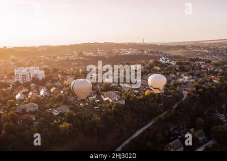Zwei Luftballons fliegen bei Sonnenaufgang über dem grünen Park und der kleinen europäischen Stadt. Stockfoto