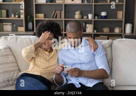 Verärgerte afrikanische Frau fühlt sich unzufrieden mit Ehemann Smartphone sucht Stockfoto