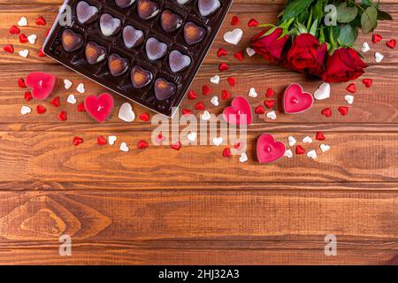 Valentinstag Konzept Schokolade Bonbons herzförmig und rote Rosen mit Kerzen auf Holz. Liebe und Romantik Konzept. Stockfoto