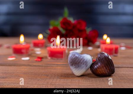 Valentinstag Konzept Schokolade Bonbons herzförmig und rote Rosen mit Kerzen auf Holz. Liebe und Romantik Konzept. Stockfoto