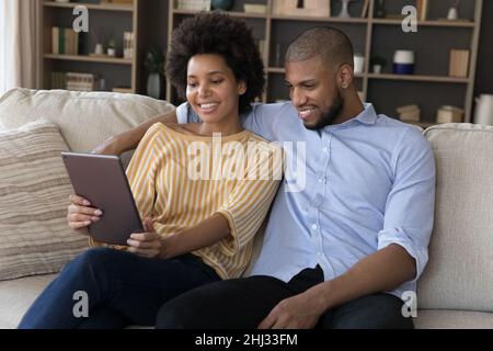Schönes afrikanisches Paar, das sich mit einem digitalen Tablet auf dem Sofa entspannt Stockfoto