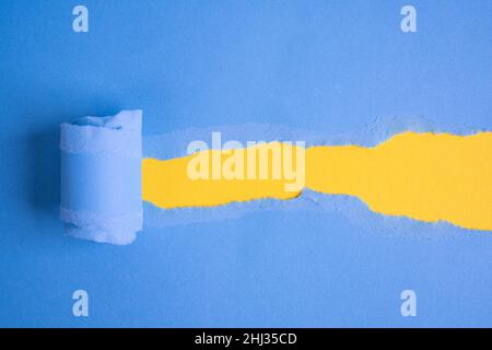 Ein zerrissenes blaues Blatt Papier, das ein Fenster auf einem gelben Hintergrund öffnet Stockfoto