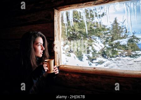 Frau mit einer Tasse Tee blickt im Winter aus dem Fenster Stockfoto