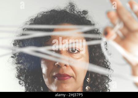 Nahaufnahme des Gesichts einer Frau, die ein farbenfrohes Kleid mit Kordelzug in den Händen vor hellgrauem Hintergrund trägt. Salvador, Bahia, Brasilien. Stockfoto