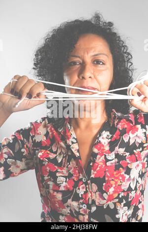 Nahaufnahme des Gesichts einer Frau, die ein farbenfrohes Kleid mit Kordelzug in den Händen vor hellgrauem Hintergrund trägt. Salvador, Bahia, Brasilien. Stockfoto